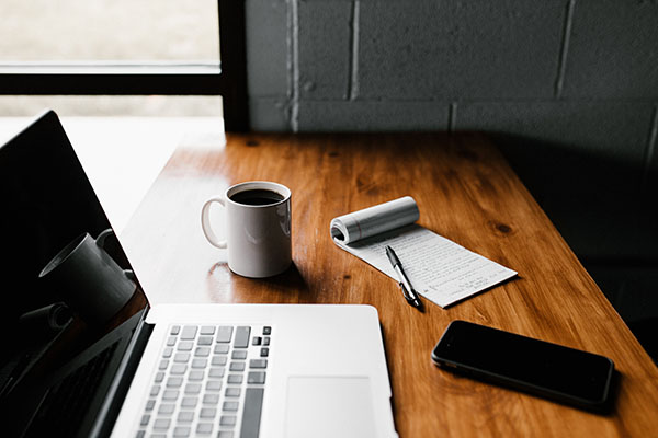 Ordinateur posé sur une table avec un calepin, une tasse de café et un téléphone